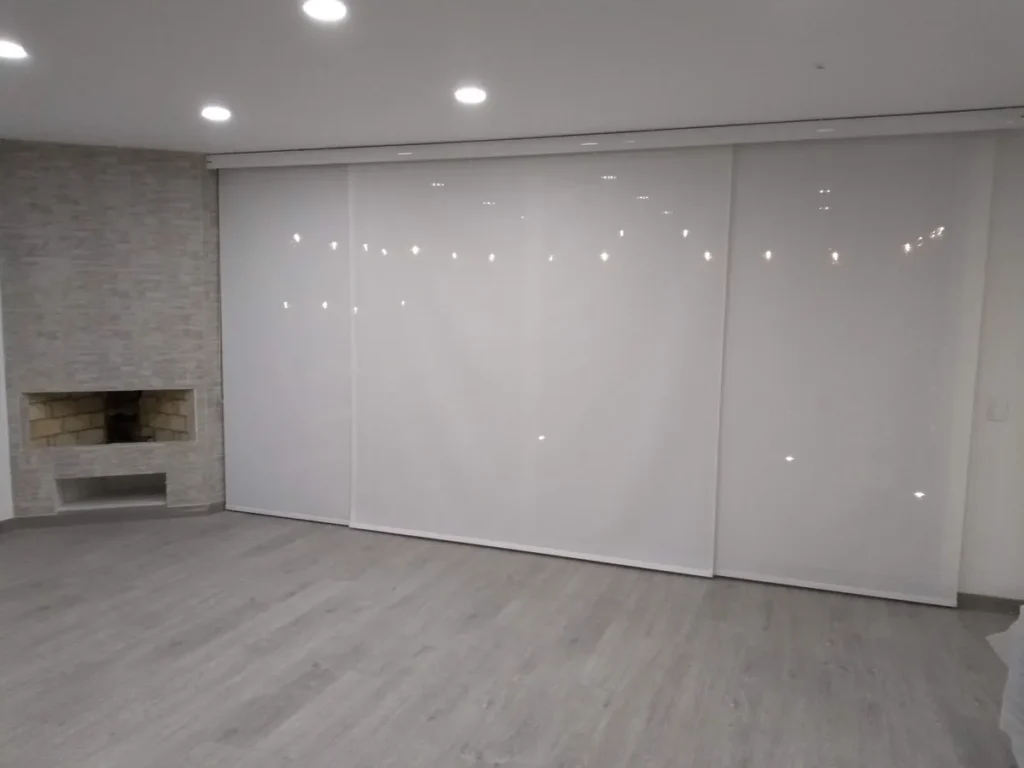 Tres cortinas enrollables screen cubriendo un ventanal amplio junto a una chimenea